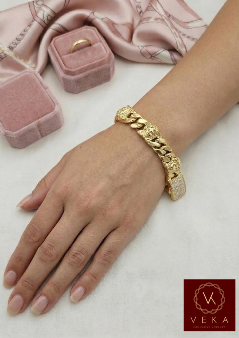 Woman wearing a thick 15mm 10K yellow gold Cuban link bracelet with Medusa head details and a sparkling CZ clasp on her wrist