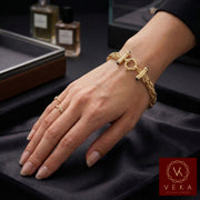 A close-up of a woman's hand resting on black velvet, wearing a 10K yellow gold 8mm Byzantine link bracelet and thin gold rings.