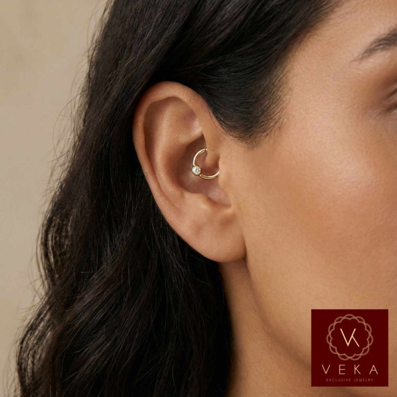 Close-up of an ear wearing a gold cartilage bezel piercing with Veka Jewelry logo in the corner.