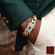 A close-up of a person's wrist wearing a Monaco 10K Real gold chain bracelet with a textured white a Pave Lock with The Monaco logo. The person is wearing a dark green blazer and off-white trousers, with a Veka brand watermark in the bottom right corner.