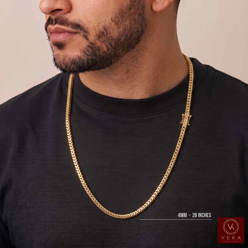 A cropped torso photo of a man with a beard wearing the 4mm 14K yellow gold hollow Franco chain necklace over a black t-shirt. The chain is draped low around his neck. A Veka logo is visible in the corner.