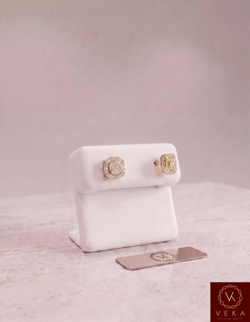 Pair of men's 10K yellow gold square moissanite stud earrings on a white display stand by Veka Jewelry.