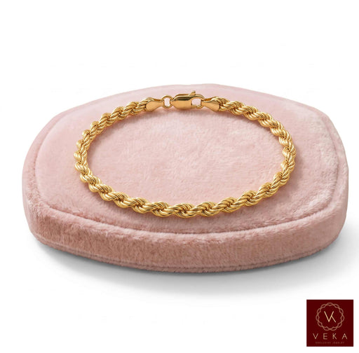 A solid 10k Real gold rope-style bracelet displayed on a round blush pink velvet jewelry stand against a clean white background, with a Veka Jewelry logo in the bottom right corner.