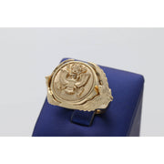 A heavy men's 14k yellow gold ring featuring an embossed Great Seal of the United States on a shield face and sculpted eagles on the sides, resting on a blue display stand.