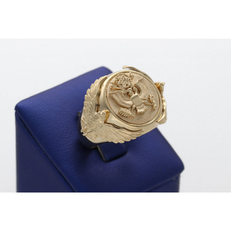 A heavy men's 14k yellow gold ring featuring an embossed Great Seal of the United States on a shield face and sculpted eagles on the sides, resting on a blue display stand.