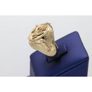 A heavy men's 14k yellow gold ring featuring an embossed Great Seal of the United States on a shield face and sculpted eagles on the sides, resting on a blue display stand.