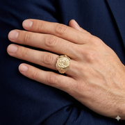 A male model's hand wearing the massive 14k gold Great Seal eagle shield ring on the ring finger, resting against a dark blue suit jacket sleeve.