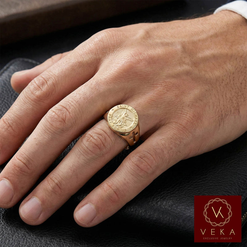 A male model's hand wearing the 14K gold Saint Michael signet ring on the ring finger, resting on a black leather wallet