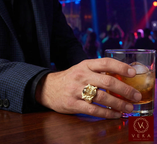 A stylish man wearing the Veka Jewelry 10K yellow gold Viking warrior ring on his finger while holding a drink in a dimly lit, upscale night club. The ring features black synthetic ruby stones and a detailed Norse helmet design.