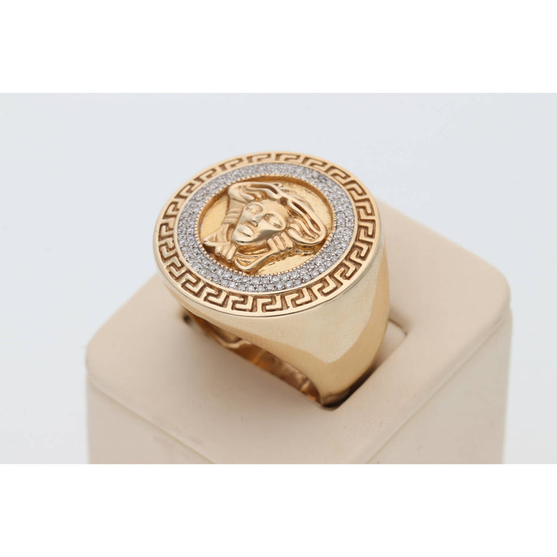 A side profile view of the Veka Jewelry men's gold Medusa ring, showcasing the high-polish finish of the solid 10k gold band and the substantial depth of the ring face. The ring is presented on a minimalist beige cylindrical display pedestal against a neutral white background.