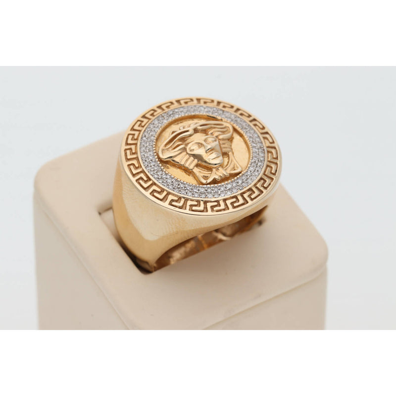 An elevated three-quarter view of the Veka Jewelry 10k gold and 1/3 ctw natural diamond Medusa ring for men, showing the top face and a curve of the band. The detailed gold relief and sparkling pavé halo are displayed on a simple, cream-colored jewelry stand