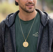 Male model wearing a two-tone gold Saint Benedict pendant on a long chain with casual sportswear