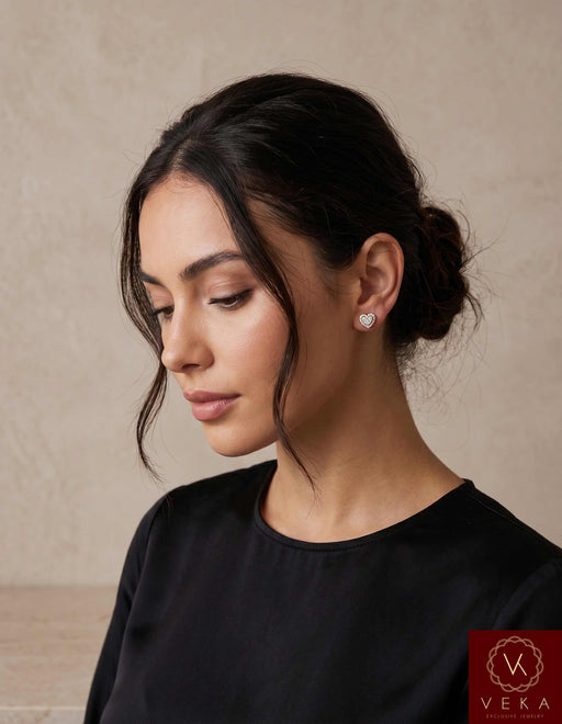 Elegant woman wearing 7mm 10K gold moissanite heart stud earrings with a neutral background.