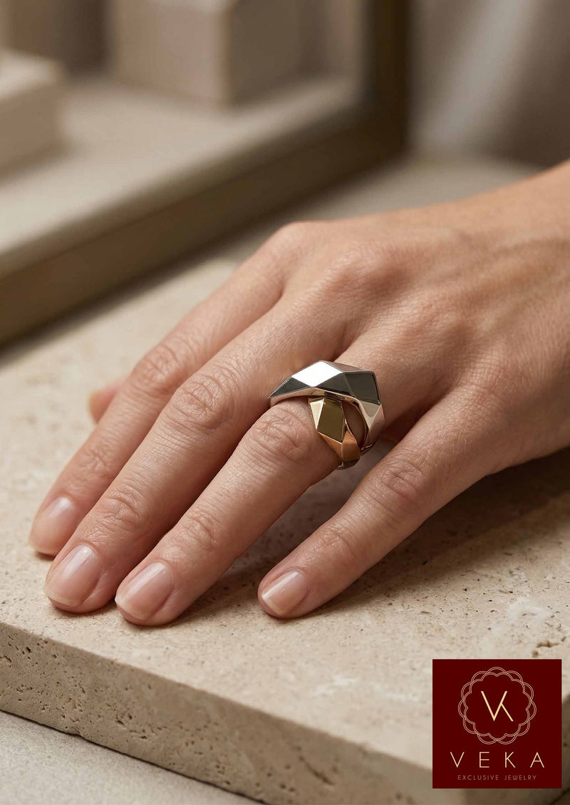 Model wearing a bold architectural X-shaped statement ring in solid 14k yellow and white gold on a minimalist stone background