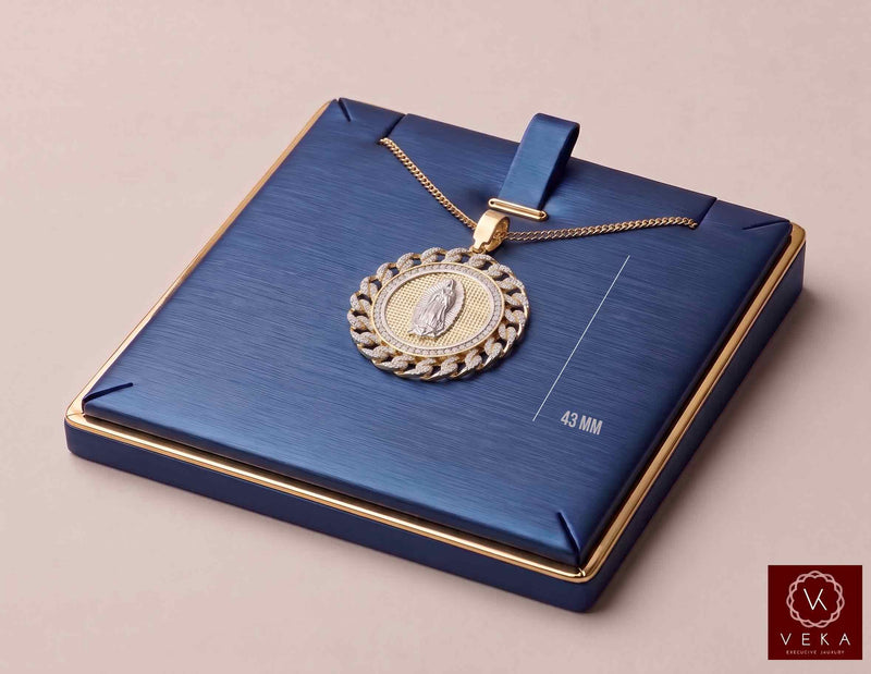 A detailed three-quarter view of the Veka Jewelry 14K Gold Virgen de Guadalupe Medallion Pendant, featuring a pave CZ frame, resting on a sophisticated, rich blue presentation box with a matching gold chain.