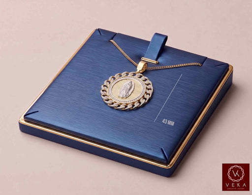 A detailed three-quarter view of the Veka Jewelry 14K Gold Virgen de Guadalupe Medallion Pendant, featuring a pave CZ frame, resting on a sophisticated, rich blue presentation box with a matching gold chain.