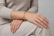 Model wearing a 14K yellow gold 4mm screw motif hollow bangle bracelet on wrist, Veka Jewelry Orlando FL.