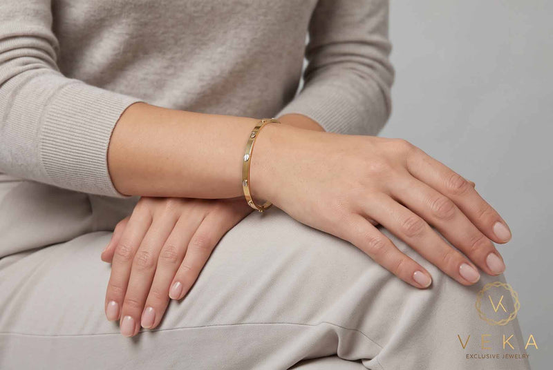 Model wearing a 14K yellow gold 4mm screw motif hollow bangle bracelet on wrist, Veka Jewelry Orlando FL.