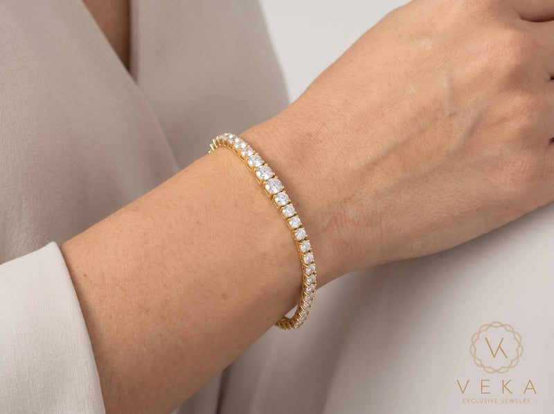 Lifestyle view of a woman wearing the 14K yellow gold graduated tennis bracelet on her wrist showcasing natural drape and 2.5mm to 5mm width proportion - Veka Jewelry.