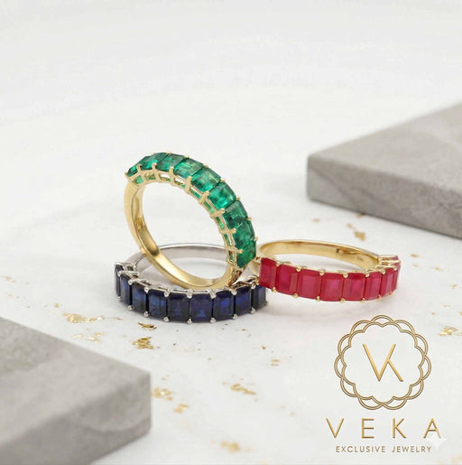 Trio of VEKA 14K gold eternity rings with emerald cut natural gemstones: green emerald, blue sapphire, and red ruby.