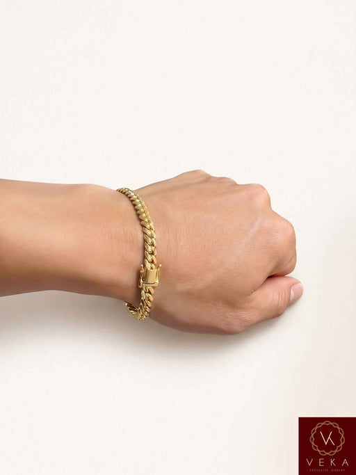 Man wearing a VEKA Jewelry 6mm 14K solid yellow gold Miami Cuban link bracelet on his wrist against a soft white beige background