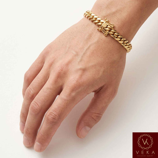 Man wearing a VEKA Jewelry 8mm 14K solid yellow gold Miami Cuban link bracelet on his wrist against a soft white beige background