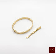 Elegant yellow gold screw bangle bracelet paired with its matching precision screwdriver on a white background by Veka Jewelry.
