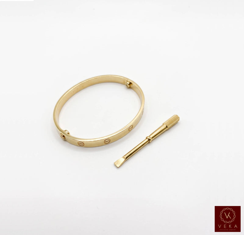 Elegant yellow gold screw bangle bracelet paired with its matching precision screwdriver on a white background by Veka Jewelry.