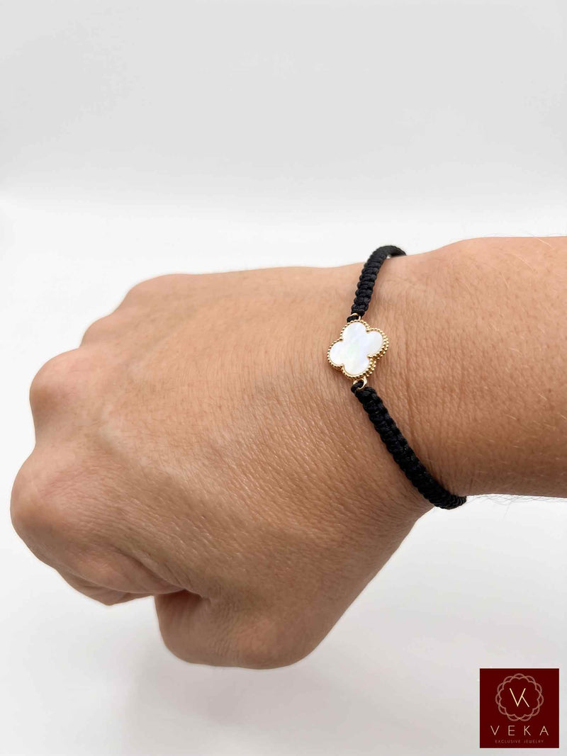 Close-up view of a woman wearing the VEKA Jewelry gold mother of pearl clover bracelet with a black woven macrame cord