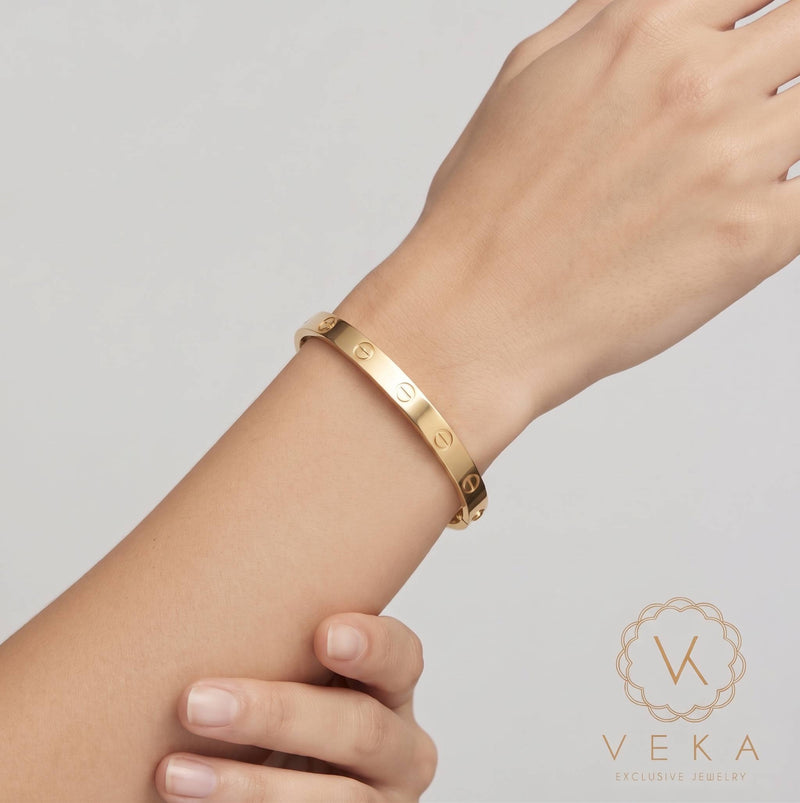Female model gracefully wearing a classic yellow gold screw bangle bracelet on her wrist for Veka Jewelry