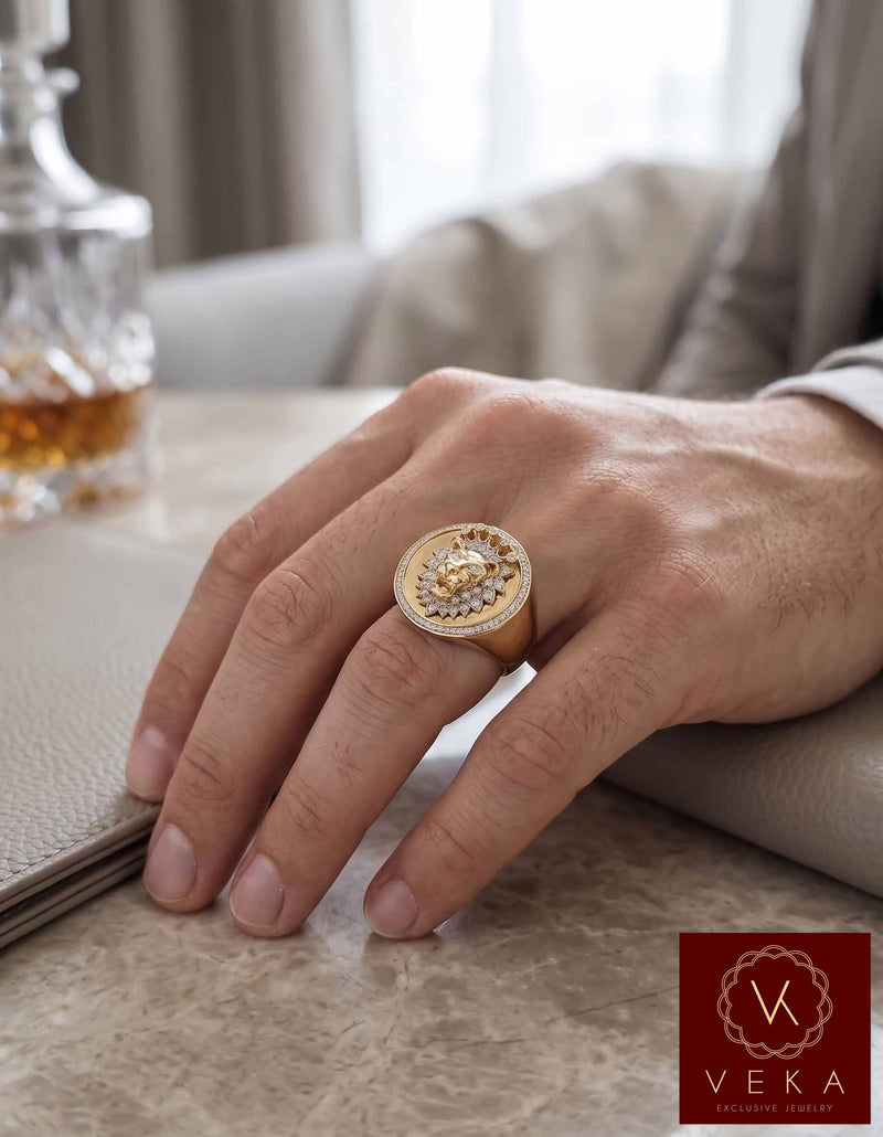 VEKA Exclusive Jewelry: Close-up on a man's hand wearing a large, ornate 14k yellow gold and diamond lion face signet ring, set against a luxurious lifestyle background with a leather mat and crystal