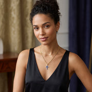 Female model styling a 14K yellow gold cross pendant featuring blue enamel and cubic zirconia on layered gold chains