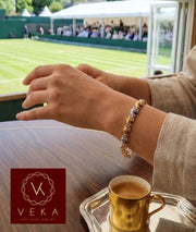 A woman wearing a 14K tri-color gold elephant bracelet on her wrist at a luxury sporting event (Wimbledon) with a gold espresso cup on the table.