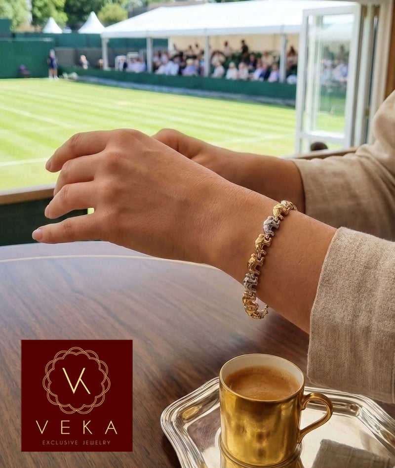 A woman wearing a 14K tri-color gold elephant bracelet on her wrist at a luxury sporting event (Wimbledon) with a gold espresso cup on the table.