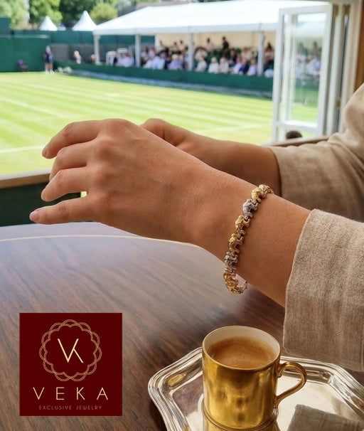 A woman wearing a 14K tri-color gold elephant bracelet on her wrist at a luxury sporting event (Wimbledon) with a gold espresso cup on the table.