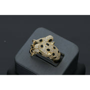 A 14 karat gold ring designed with a leopard motif, featuring small stones including green stones and a gold chain from face to tail on a dark background showing also black spots on the leopard.