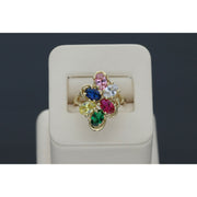 Graceful 14 karat Gold Multicolor Floral Ring 2025 Jewelry design with vibrant Sapphire accents, set on a beige ring holder in a gray backround.